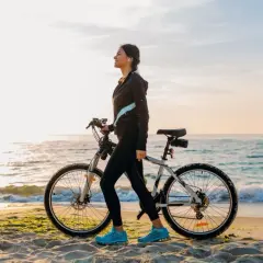 Kobieta z rowerem na plaży, idealna na trasę rowerową Władysławowo Hel. Słońce, morze i piasek tworzą malowniczy krajobraz.