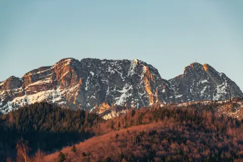 Giewont w słońcu, z ośnieżonymi zboczami i lasem u podnóża. Jego imponująca wysokość robi wrażenie.