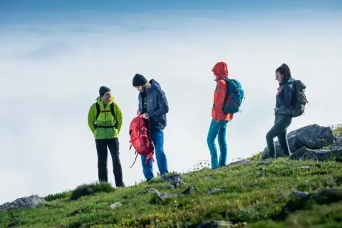 Cztery osoby w górskim krajobrazie, przygotowujące się do wyprawy. To właśnie jest trekking – przygoda na szlaku!