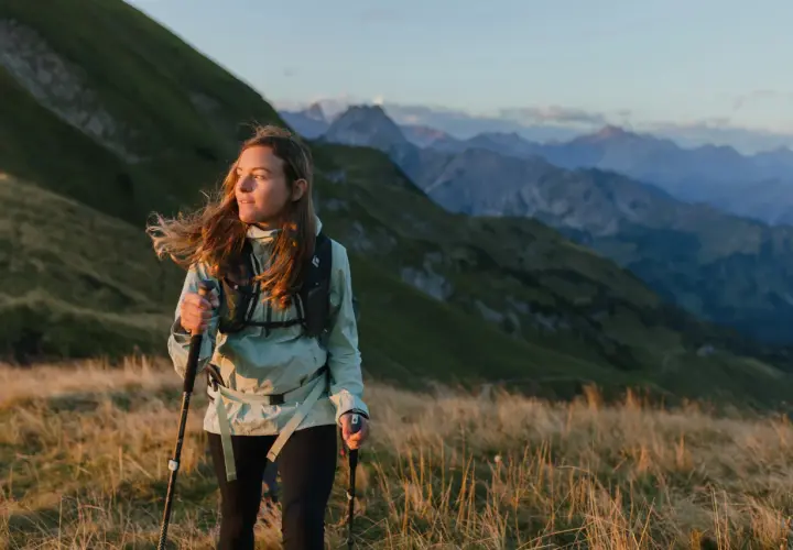 Kobieta z kijkami do **speed hikingu** podziwia alpejski krajobraz o zachodzie słońca.