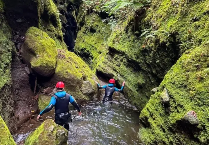 Dwie osoby w kombinezonach i kaskach przemierzają wąski, porośnięty mchem kanion. To właśnie jest canyoning!