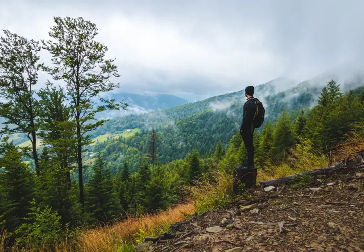 Mężczyzna z plecakiem podziwia widok na górzyste tereny podczas **hiking po polsku**. Mgła spowija szczyty, tworząc malowniczy krajobraz.