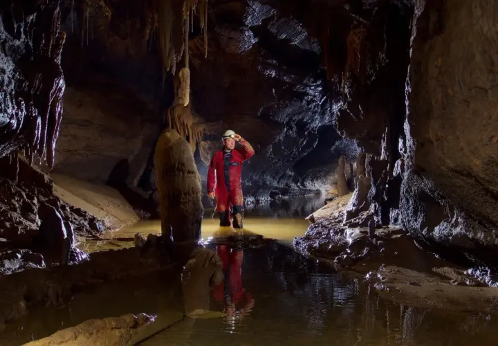 Eksplorator w czerwonym kombinezonie w jaskini z wodą. To jest właśnie speleologia – co to za fascynująca przygoda!