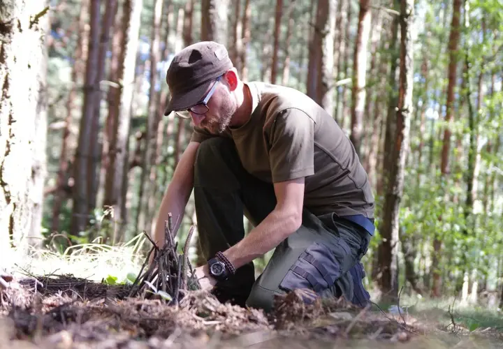 Mężczyzna w lesie przygotowuje rozpałkę. To pokazuje, survival co to znaczy: umiejętność radzenia sobie w trudnych warunkach.
