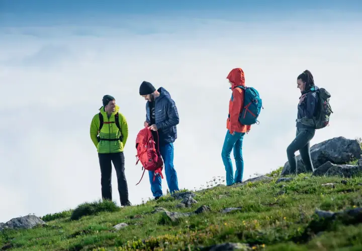 Cztery osoby w górskim krajobrazie, przygotowujące się do wyprawy. To właśnie jest trekking – przygoda na szlaku!