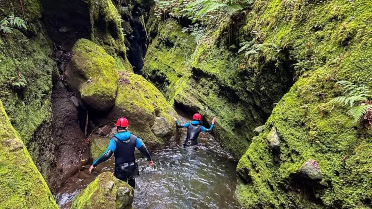 Dwie osoby w kombinezonach i kaskach przemierzają wąski, porośnięty mchem kanion. To właśnie jest canyoning!
