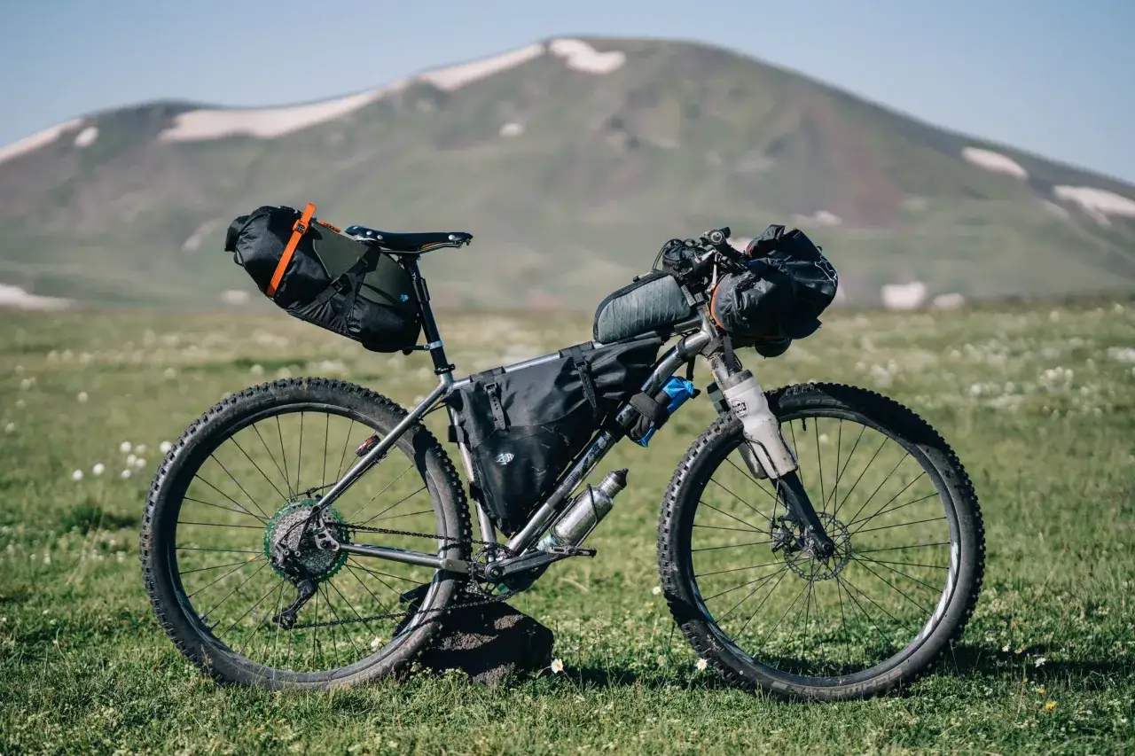 Rower gotowy do bike packingu, obładowany sakwami, stoi na łące z widokiem na górzysty krajobraz.