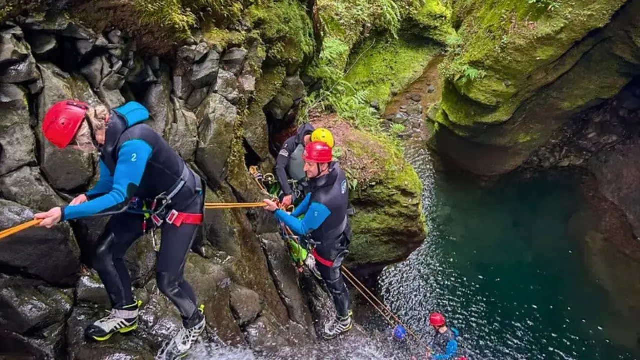 Grupa osób w kombinezonach zjazdowych pokonuje wodospad. To właśnie canyoning co to za przygoda!